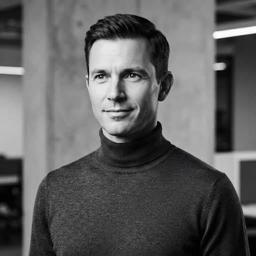 Editorial black and white studio portrait of a male principal software engineer with short hair, wearing a dark minimal turtleneck against a clean neutral architectural backdrop, illuminated with sharp studio lighting, high contrast aesthetic.